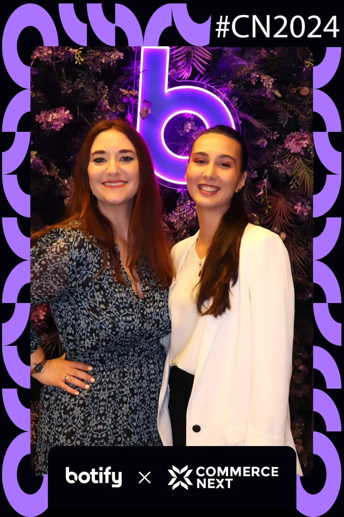 Two attendees smiling at the Botify x CommerceNext purple neon flower wall